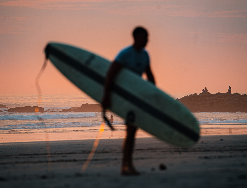 Surfer walking on the beach at sunset in Santa Teresa, Costa Rica